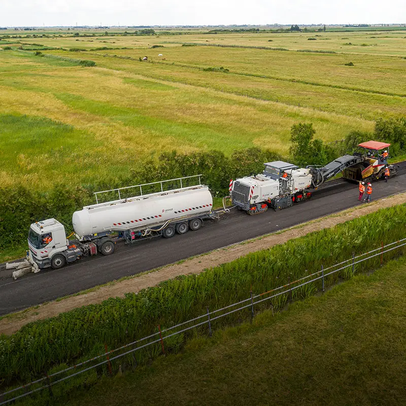 maquinaria-asfaltado-sostenible-conservacion-carreteras-espana Vista aérea de maquinaria extendiendo asfalto sostenible en una carretera en España para su conservación viaria
